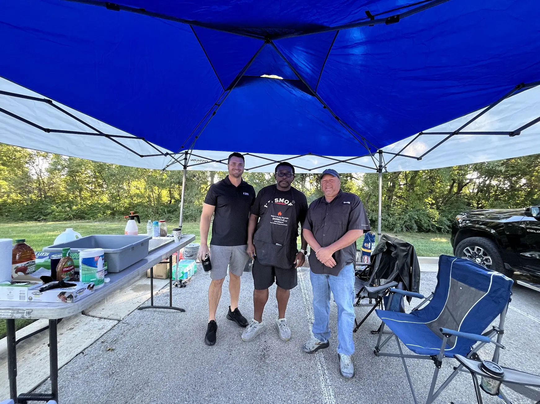 Three team members under the competition tent at the smoker station